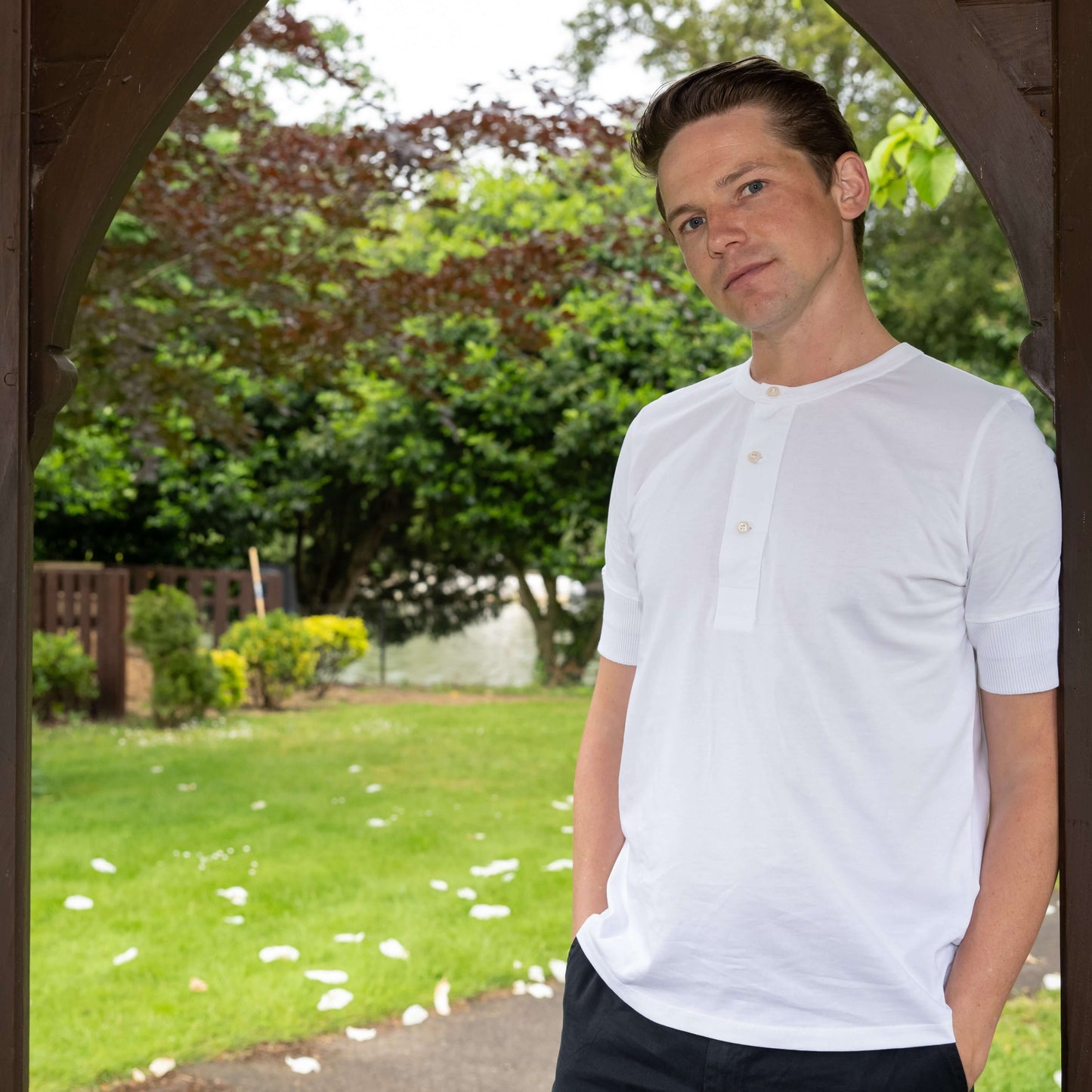 Male model standing under wooden arch wearing a white Life Scholar Henley T-Shirt.