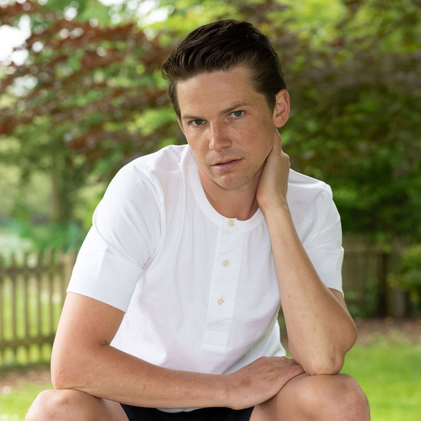 Male model sitting wearing a white Life Scholar Henley T-Shirt.